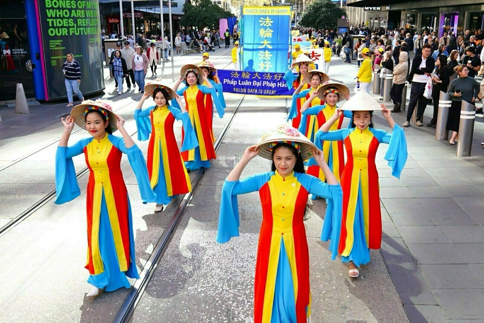 A group of people wearing colorful traditional outfits and hats are marching in a parade, holding a large banner.