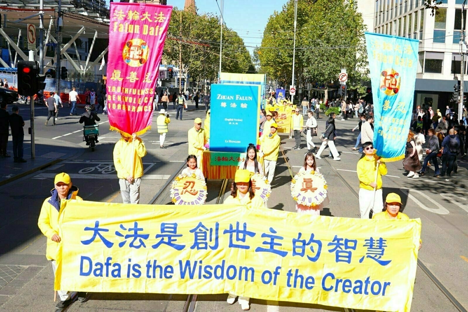 A group of people is participating in a parade, holding banners with colorful designs and text promoting Falun Dafa.
