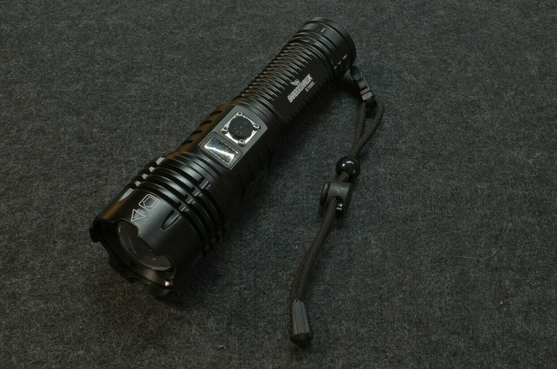 A black flashlight with a strap is resting on a dark textured surface.